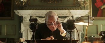 Movie still from “Churchill” (2017), directed by Jonathan Teplitzky – An older man sitting at a desk with a microphone; Close Up shot, Low angle
