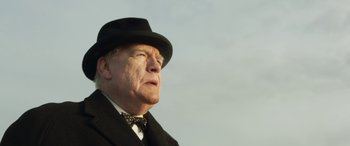 Movie still from “Churchill” (2017), directed by Jonathan Teplitzky – An older man wearing a hat and a bow tie; Close Up shot, Low angle