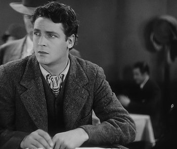 Movie still from “City Girl” (1930), directed by F.W. Murnau – A young man sitting at a table in front of other people; Medium shot, Over the shoulder angle