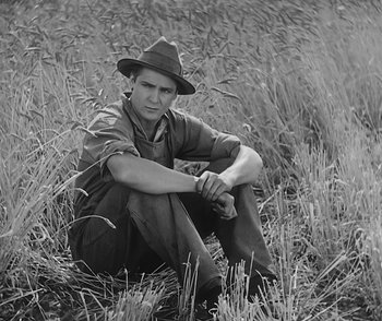 Movie still from “City Girl” (1930), directed by F.W. Murnau – A man sitting in tall grass wearing a hat; Medium shot, High angle