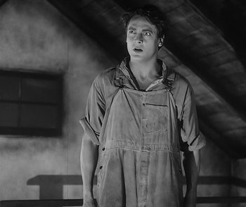 Movie still from “City Girl” (1930), directed by F.W. Murnau – A young man in an overalls is standing in a room; Medium shot, Low angle