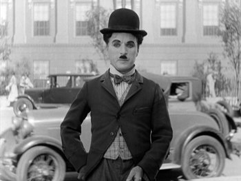 Movie still from “City Lights” (1931), directed by Charles Chaplin – A black and white photo of a man in a suit and tie; Medium shot, Low angle
