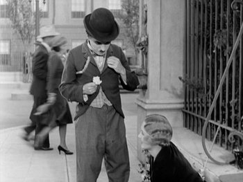Movie still from “City Lights” (1931), directed by Charles Chaplin – An old photo of a man and a woman on the sidewalk; Medium shot, Over the shoulder angle