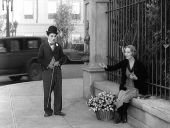 Movie still from “City Lights” (1931), directed by Charles Chaplin – A man and a woman sitting on a bench on the sidewalk; Wide shot, High angle