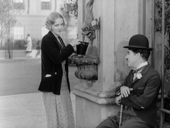 Movie still from “City Lights” (1931), directed by Charles Chaplin – A man and a woman standing in front of a fountain; Medium shot, High angle