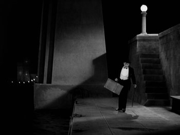 Movie still from “City Lights” (1931), directed by Charles Chaplin – A man in a suit and tie holding a briefcase walking down a street; Extreme Wide shot, Low angle