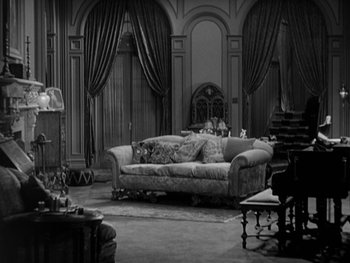 Movie still from “City Lights” (1931), directed by Charles Chaplin – A black and white photo of a living room with couches; Wide shot, High angle