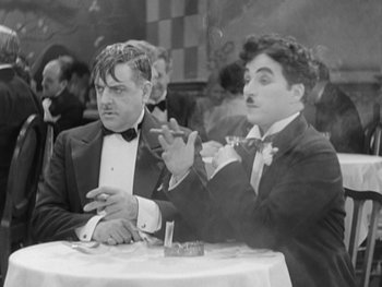 Movie still from “City Lights” (1931), directed by Charles Chaplin – A couple of men sitting at a dinner table; Medium shot, Over the shoulder angle