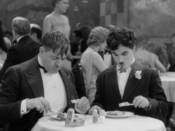 Movie still from “City Lights” (1931), directed by Charles Chaplin – A couple of men sitting at a table eating food; Medium shot, High angle