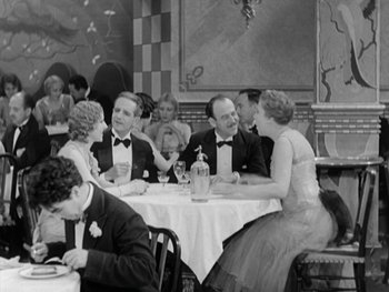 Movie still from “City Lights” (1931), directed by Charles Chaplin – A black and white photo of people sitting at a table; Wide shot, High angle