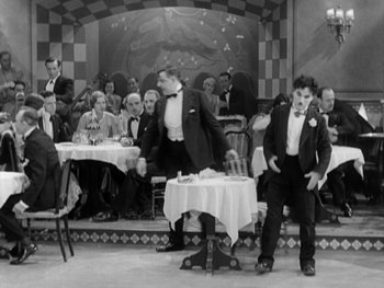 Movie still from “City Lights” (1931), directed by Charles Chaplin – A group of people sitting around a dinner table; Wide shot, High angle