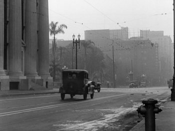Movie still from “City Lights” (1931), directed by Charles Chaplin – An old car driving down a street past tall buildings; Extreme Wide shot, Low angle
