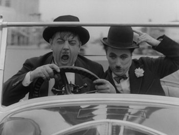 Movie still from “City Lights” (1931), directed by Charles Chaplin – A couple of men sitting in the back seat of a car; Medium shot, Low angle