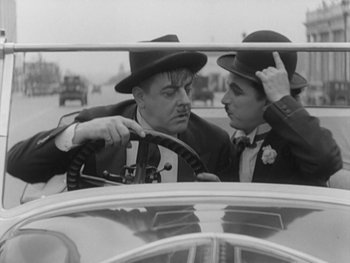 Movie still from “City Lights” (1931), directed by Charles Chaplin – A couple of men sitting in the back seat of a car; Medium shot, Low angle