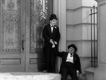Movie still from “City Lights” (1931), directed by Charles Chaplin – A couple of men standing next to each other on steps; Wide shot, High angle
