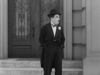 Movie still from “City Lights” (1931), directed by Charles Chaplin – An old photo of a man standing in front of a door; Medium shot, Low angle
