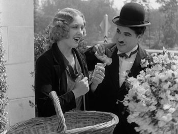 Movie still from “City Lights” (1931), directed by Charles Chaplin – A man and a woman are holding a basket of flowers; Medium shot, Low angle