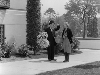 Movie still from “City Lights” (1931), directed by Charles Chaplin – An old photo of a man and a woman standing on a sidewalk; Wide shot, High angle
