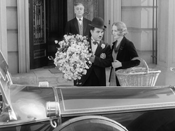 Movie still from “City Lights” (1931), directed by Charles Chaplin – A man in a top hat holding a bouquet of flowers; Medium shot, High angle
