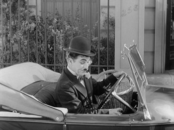 Movie still from “City Lights” (1931), directed by Charles Chaplin – An old photo of a man driving a car; Medium shot, High angle
