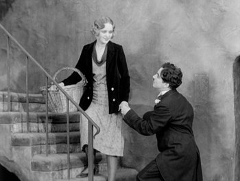 Movie still from “City Lights” (1931), directed by Charles Chaplin – An old photo of a man kneeling down on the stairs with a woman; Medium shot, High angle