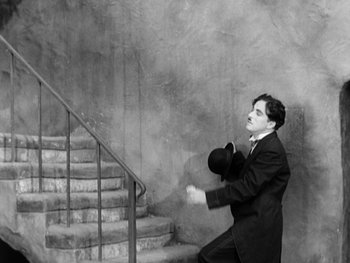 Movie still from “City Lights” (1931), directed by Charles Chaplin – A black and white photo of a man in a suit and tie; Wide shot, High angle