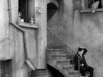 Movie still from “City Lights” (1931), directed by Charles Chaplin – A black and white photo of a man sitting on steps; Wide shot, High angle