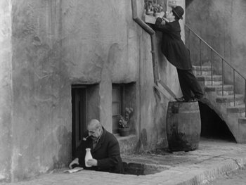 Movie still from “City Lights” (1931), directed by Charles Chaplin – A man sitting on the ground next to a man climbing up the stairs; Wide shot, Low angle