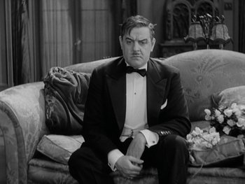 Movie still from “City Lights” (1931), directed by Charles Chaplin – A black and white photo of a man sitting on a couch wearing a tuxedo; Medium shot, High angle