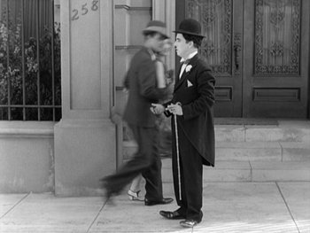 Movie still from “City Lights” (1931), directed by Charles Chaplin – A man in a top hat and a cane standing on a sidewalk; Wide shot, High angle