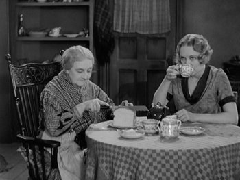 Movie still from “City Lights” (1931), directed by Charles Chaplin – Two women sitting at a table with a cake and a cup; Medium shot, High angle