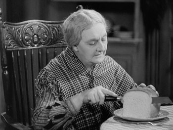 Movie still from “City Lights” (1931), directed by Charles Chaplin – An older woman cutting a cake with a knife; Close Up shot, High angle