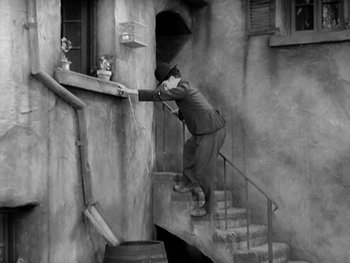 Movie still from “City Lights” (1931), directed by Charles Chaplin – A man reaching down a flight of stairs to grab something; Wide shot, High angle