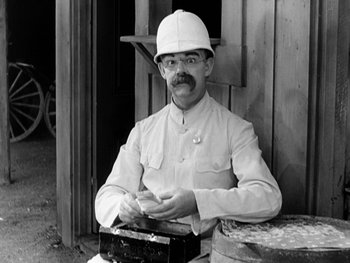 Movie still from “City Lights” (1931), directed by Charles Chaplin – A man wearing a white hat and holding a box; Medium shot, High angle