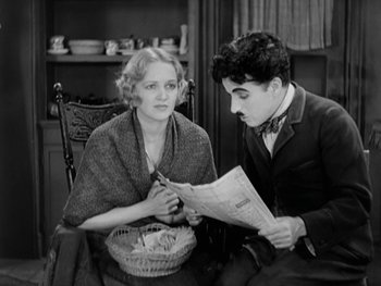 Movie still from “City Lights” (1931), directed by Charles Chaplin – A man and a woman sitting in a chair looking at a newspaper; Medium shot, High angle