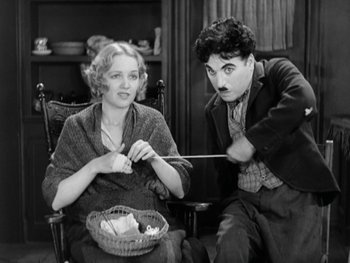 Movie still from “City Lights” (1931), directed by Charles Chaplin – An older woman sitting next to an older man in front of a basket; Medium shot, High angle