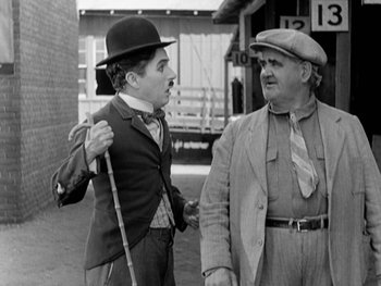 Movie still from “City Lights” (1931), directed by Charles Chaplin – A man and a man wearing a hat and holding hands; Medium shot, Low angle