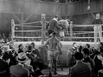 Movie still from “City Lights” (1931), directed by Charles Chaplin – An old photo of a boxing match in a boxing ring; Wide shot, Low angle