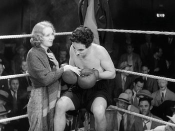 Movie still from “City Lights” (1931), directed by Charles Chaplin – An old photo of a man and a woman in a boxing ring; Medium shot, High angle