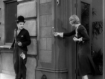 Movie still from “City Lights” (1931), directed by Charles Chaplin – A man and a woman standing in front of a building; Wide shot, Over the shoulder angle