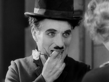 Movie still from “City Lights” (1931), directed by Charles Chaplin – An old photo of a man in a top hat smoking a cigarette; Close Up shot, High angle