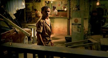 Movie still from “City of God” (2002), directed by Kátia Lund – A man standing next to a counter in a room; Wide shot, Over the shoulder angle