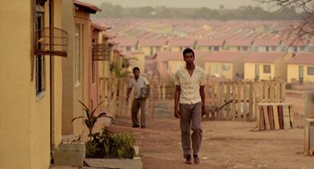 Movie still from “City of God” (2002), directed by Kátia Lund – Two men walking down a dirt path in a residential area; Wide shot, Over the shoulder angle