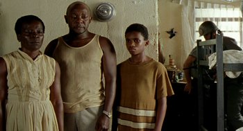 Movie still from “City of God” (2002), directed by Kátia Lund – A man standing next to a young boy in front of a wall; Medium shot, Low angle