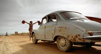 Movie still from “City of God” (2002), directed by Kátia Lund – A woman standing next to an old car on a dirt road; Wide shot, Low angle