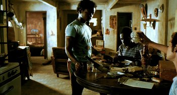 Movie still from “City of God” (2002), directed by Kátia Lund – A man standing at a table cutting food with a pair of knifes; Medium shot, Low angle