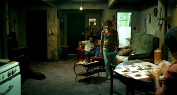 Movie still from “City of God” (2002), directed by Kátia Lund – A man standing in a living room next to a table; Wide shot, High angle