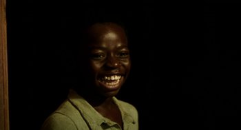 Movie still from “City of God” (2002), directed by Kátia Lund – A young boy smiling for the camera in the dark; Close Up shot, High angle