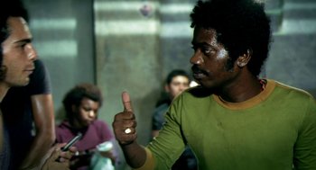 Movie still from “City of God” (2002), directed by Kátia Lund – A man giving the middle finger to the camera; Medium shot, Low angle