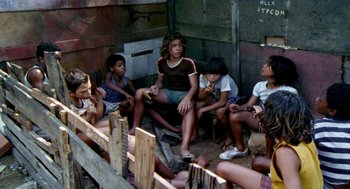 Movie still from “City of God” (2002), directed by Kátia Lund – A group of people sitting on the ground in front of a wooden fence; Wide shot, High angle